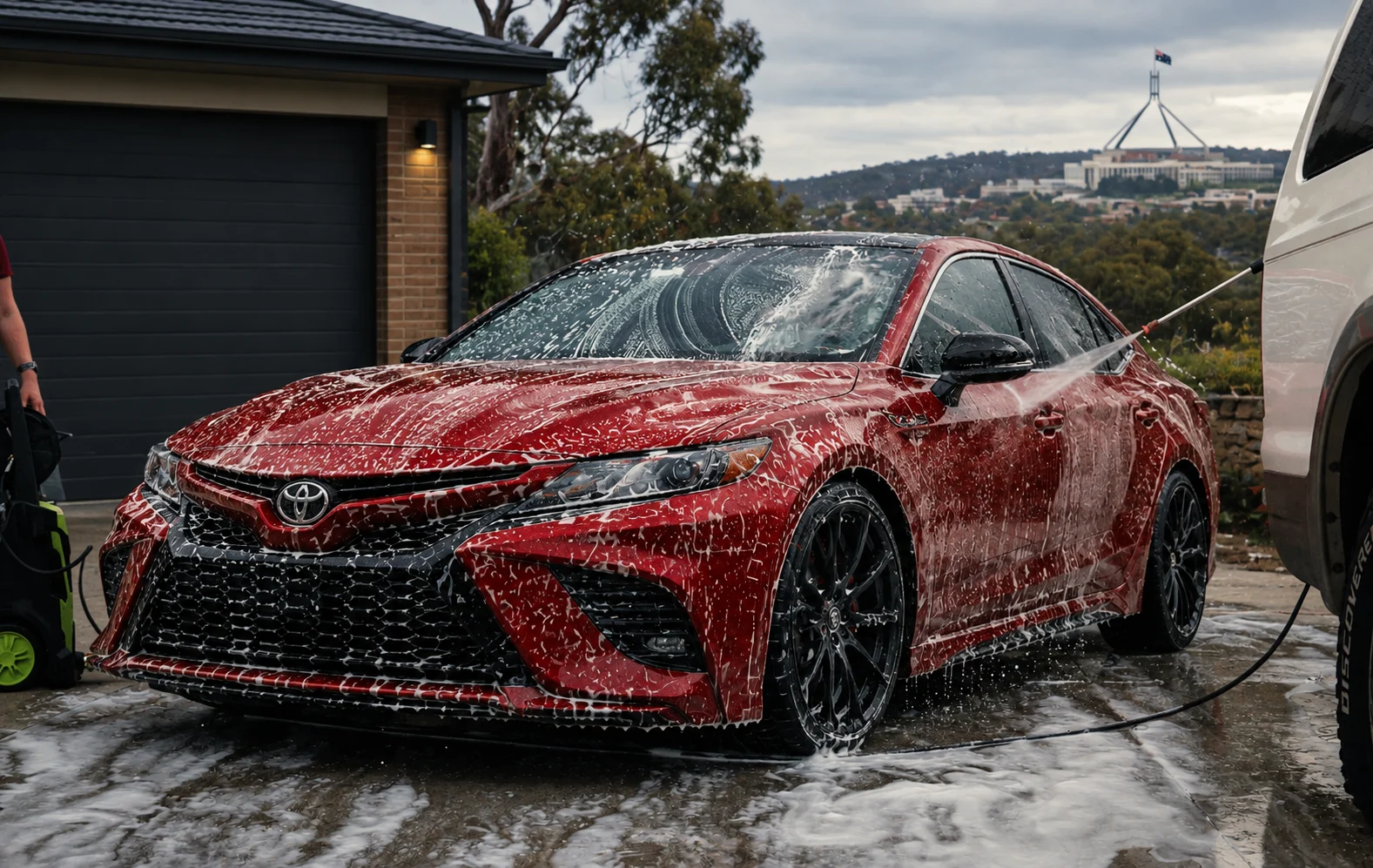 A red Toyota Camry being washed in a Canberra driveway, Parliament House behind