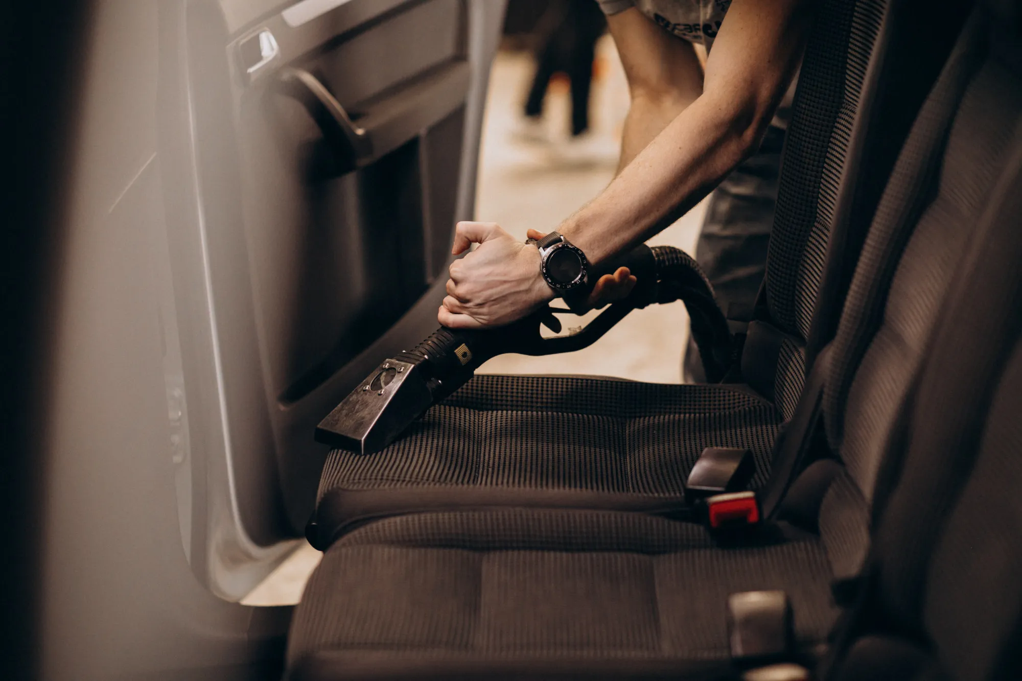 A car seat being vacuumed with a handheld vacuum